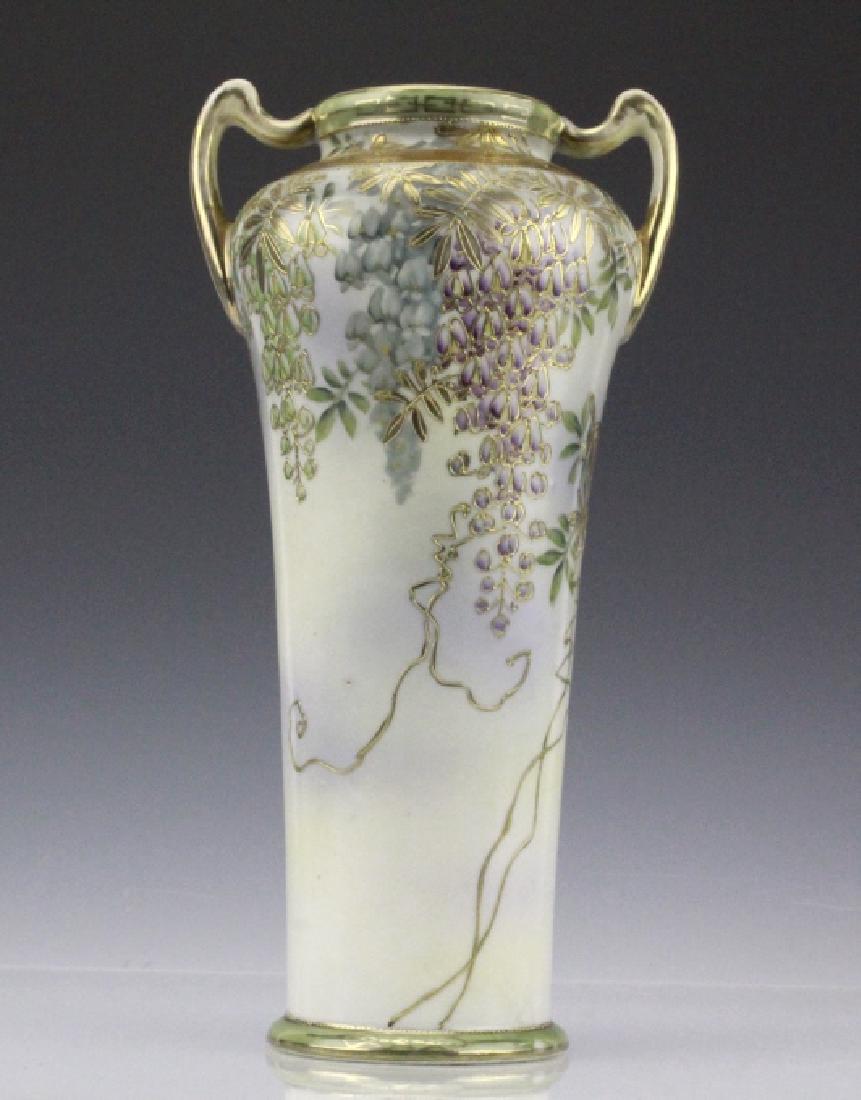 Nippon Painted Floral, Gilt Decorated Antique Vase: Antique Nippon vase. Crafted of fine Japanese porcelain. It features a cream and purple ground with hand painted blue flowers and leaves with gilt accents and leaves. Twin upturned handles connecting 
