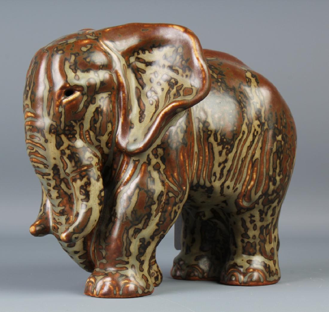 Knud Kyhn Royal Copenhagen Stoneware Elephant: Crafted of fine quality glazed stoneware pottery. Designed by Knud Kyhn (1880-1969 Denmark). Depicts an African Elephant in earth tone glaze colors. Signed with the Royal Copenhagen Blue Waves mark an