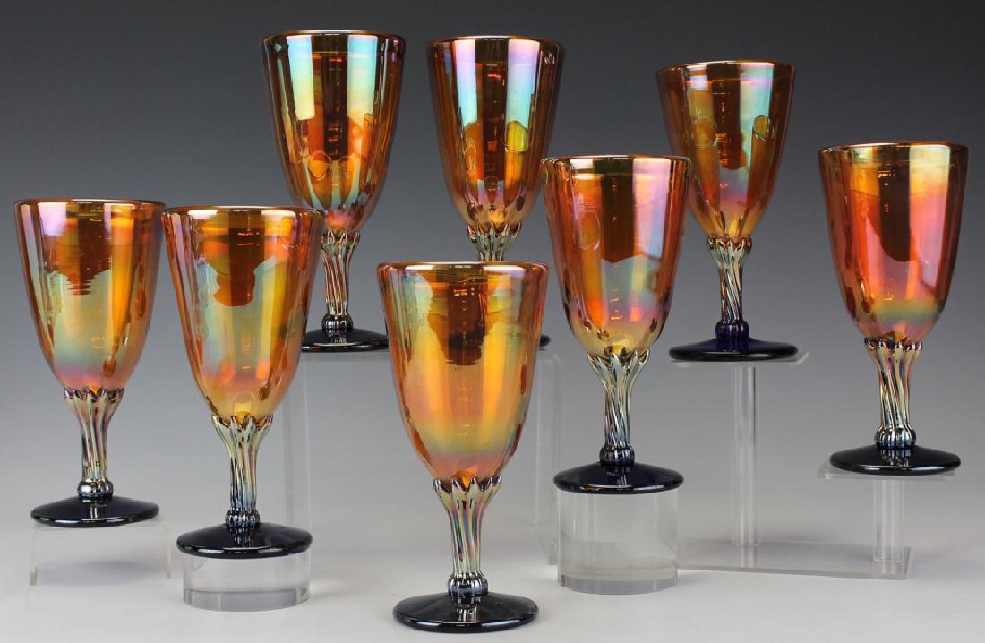 8 Rick Strini Iridescent Glass Wine Water Goblets: Set of eight (8) Rick Strini iridescent studio art glass water goblets. These goblets feature iridescent orange bowl with a fluted blue glass stem. Signed on base. Measures 6 1/2" with a 3" rim. Good 