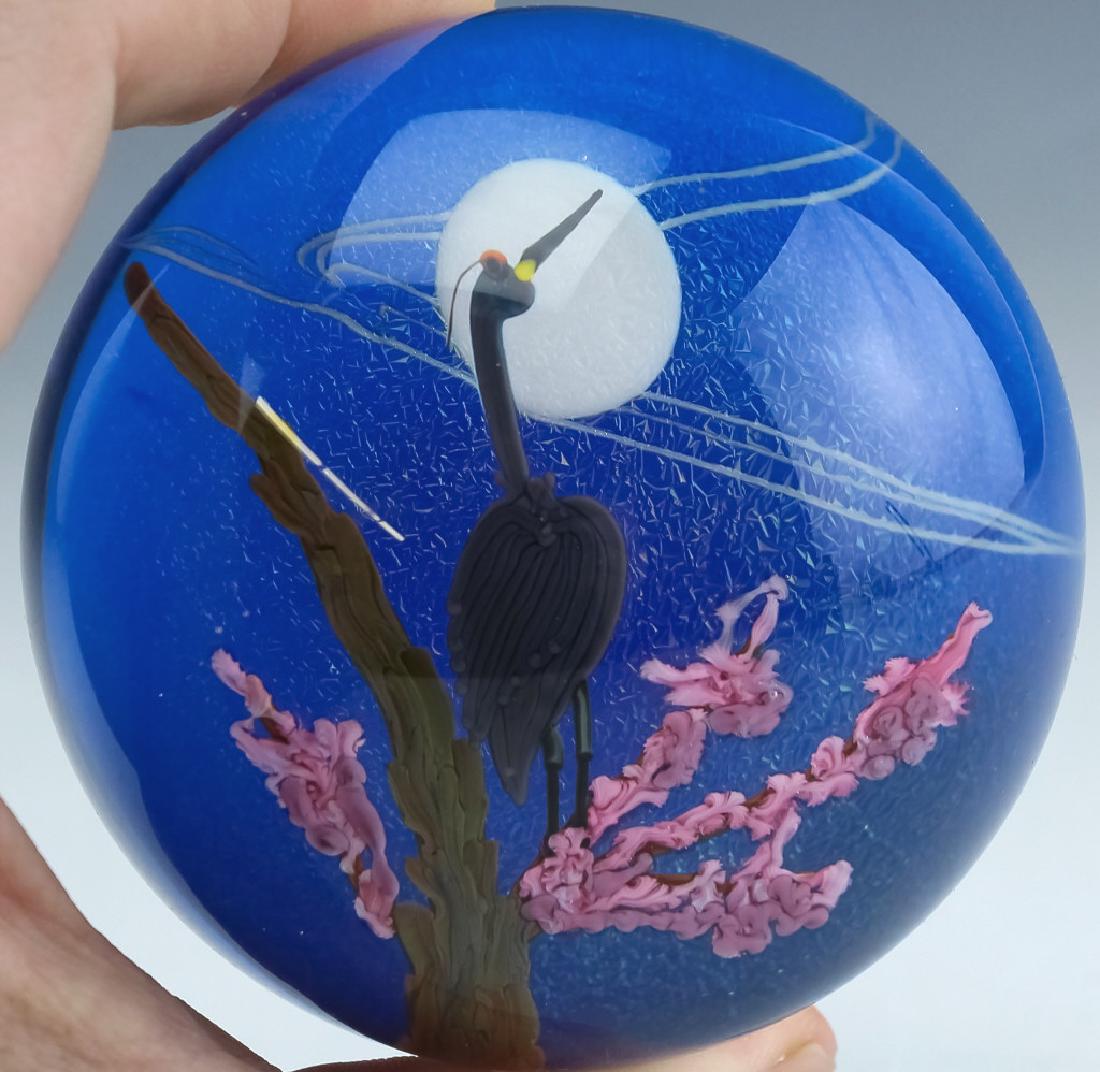 Lundberg Studio Art Glass Crane Bird Paperweight: Guaranteed Authentic. Signed limited edition Steven Lundberg studio art glass paperweight. Features a paperweight in a spherical form with a scene depicting a crane perched on a tree with pink flowers