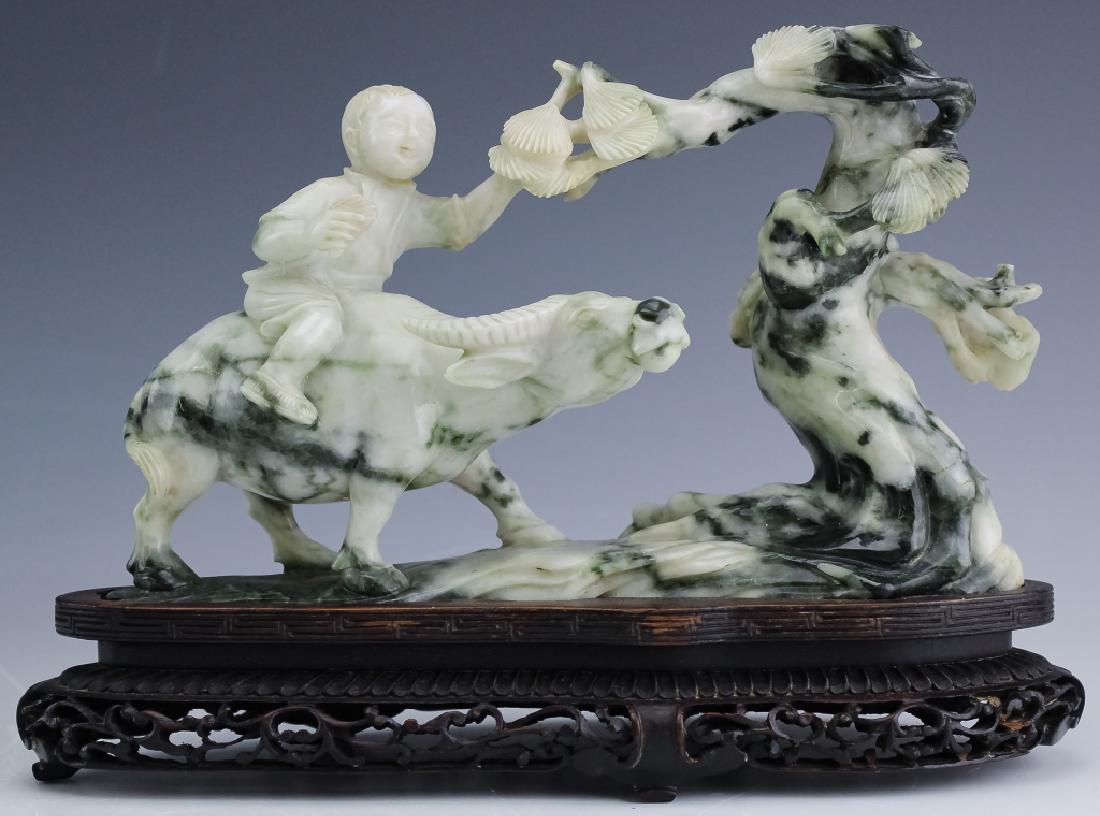 Antique Chinese Carved Figural Jade Art Sculpture: Carved Chinese figurine. Crafted from jade with green and white streaks throughout. Sculpture depicts a boy riding on the back of an oxen and grabbing a tree branch. The stone is fixed to a finely car