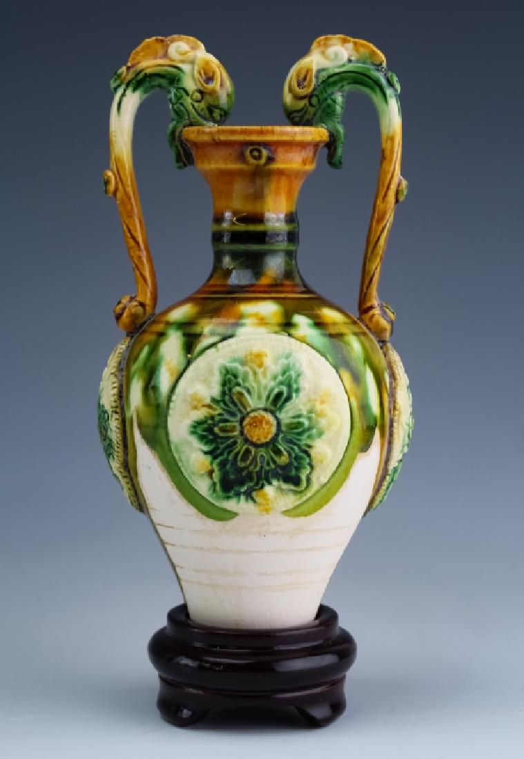 Chinese Sancai Three Color Ware Double Handle Vase: Chinese three color ware vase. Features a diminutive vase with raised floral medallion on the body as well as dragon form double handles. Fixed to a wood base. Measures 6" x 2 1/2". Good overall condi