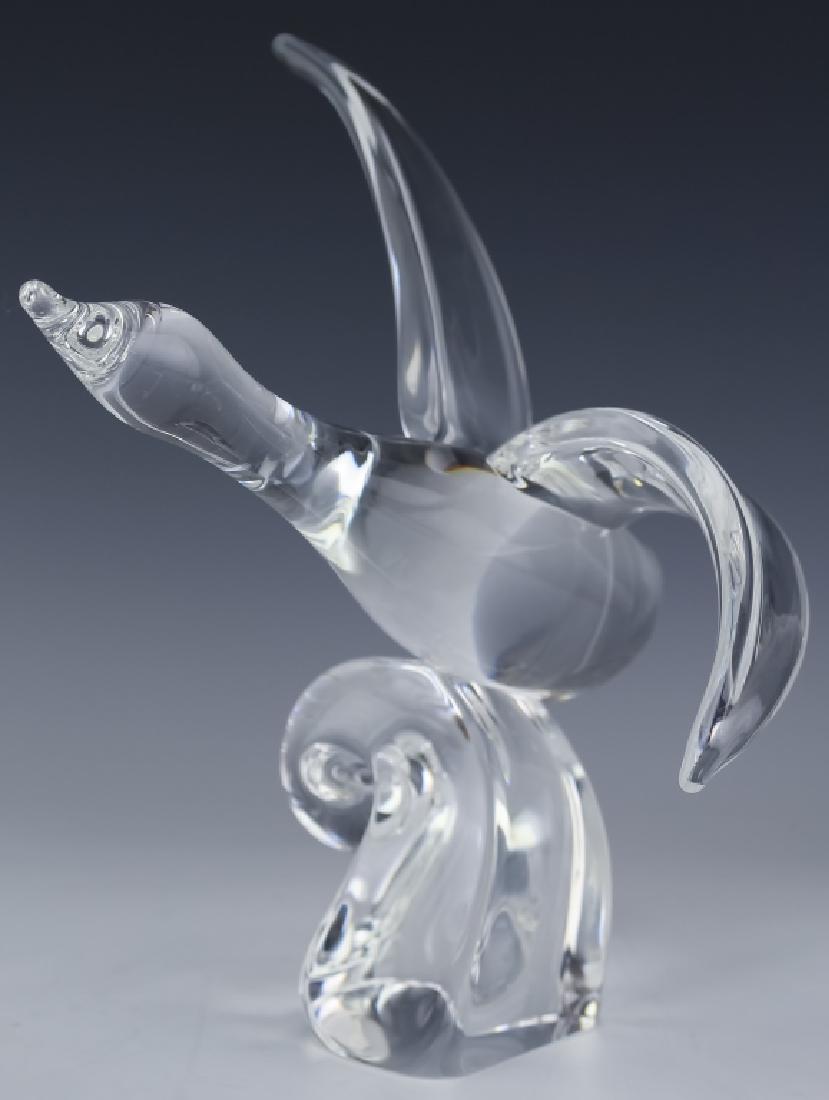 Steuben American Art Glass Crystal Goose In Flight: Steuben goose figurine. Guaranteed Authentic. Features the form of a flying goose with outstretched wings and a curled wave underneath the bird. Signed Steuben on base. Measures 10 1/4" x 6 1/2" x 9 1