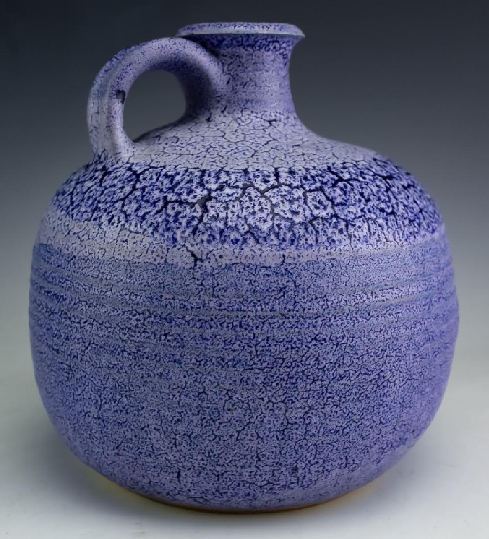 Mystery 8" Purple Art Pottery Jug DAMONE ESTATE: Studio artist signed pottery jug. Features a fat bulbous form with a purple crackled surface consistent with intent. Has a looped handle near the narrow spout. Signed on base. Measures 8 1/4" x 8". Go