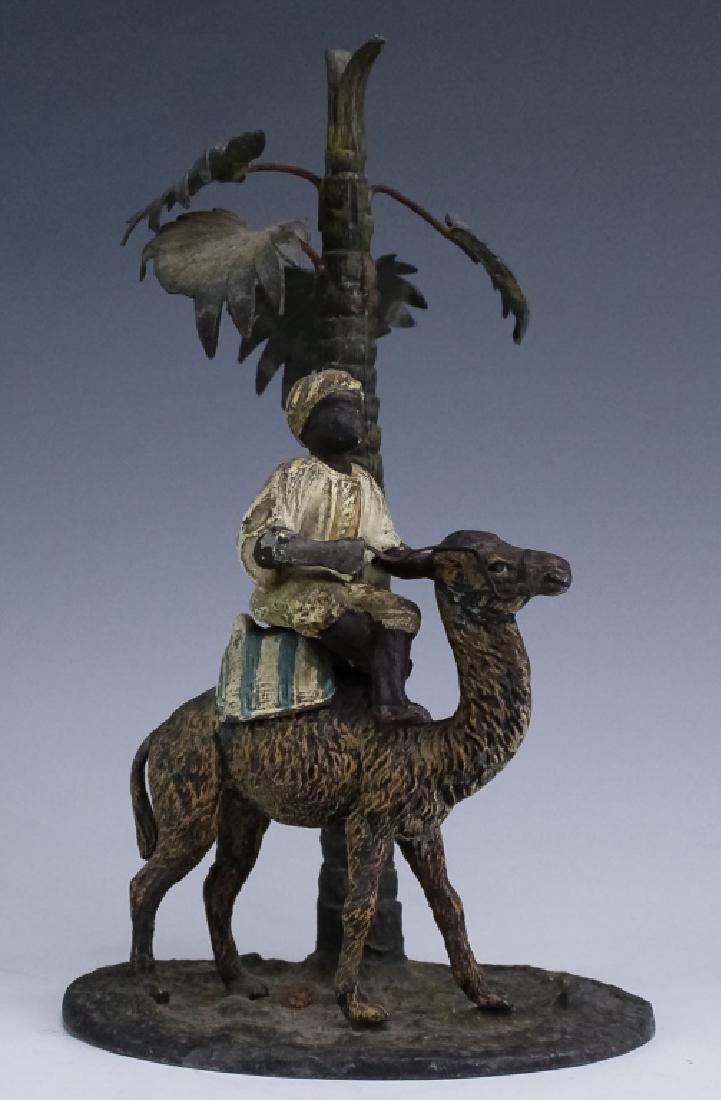 Austrian Cold Painted Spelter Orientalist Statue: Bronze type statuette in Orientalist style. Crafted of white metal with a hand painted finish. Sculpture depicts a turbaned man riding a camel underneath a palm tree. Measures 8 1/2" x 5" Fair conditi