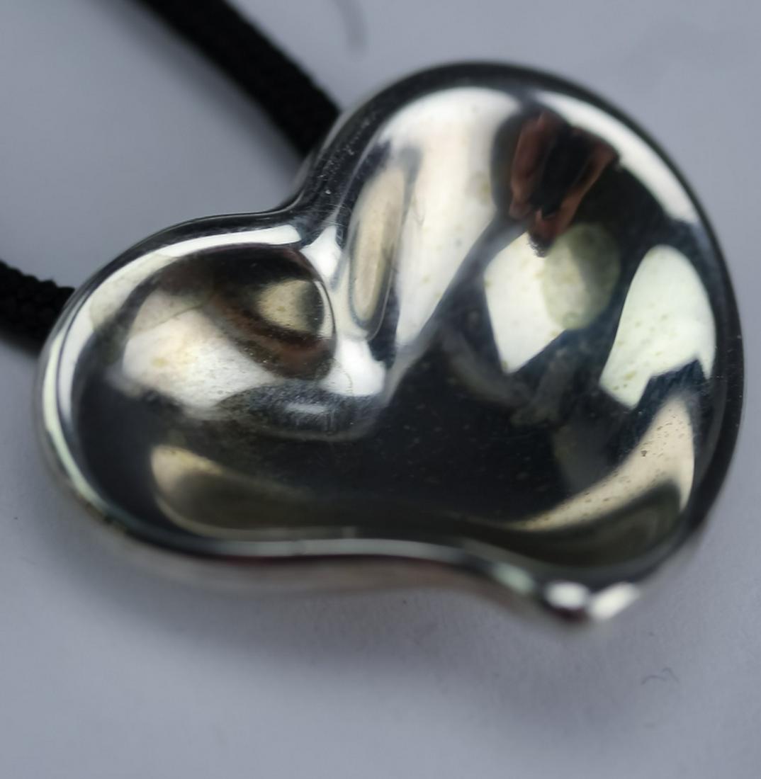 Tiffany & Co Elsa Peretti Modernist Heart Pendant: Tiffany & Co. Elsa Peretti sterling silver hear pendant and chord. Features a modernist heart pendant in silver designed by Peretti. It's strung on a black fabric chord. Heart measures 1" x 1 1/8". Ch