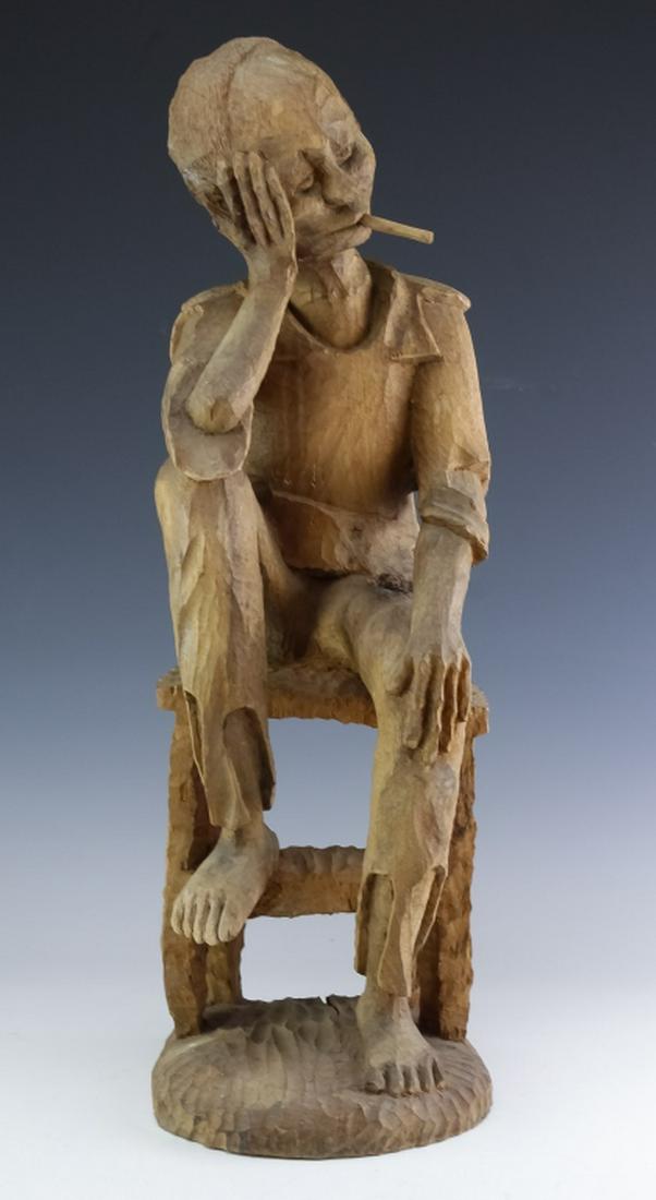 Cuban Folk Art Carved Wood Smoking Man Sculpture: Folk art carved wood sculpture of a man. Crafted from a single wood block. Features the form of a man seated with his head in his hands and a cigarette in his mouth. Unsigned. Measures 25" x 8" x 7". 