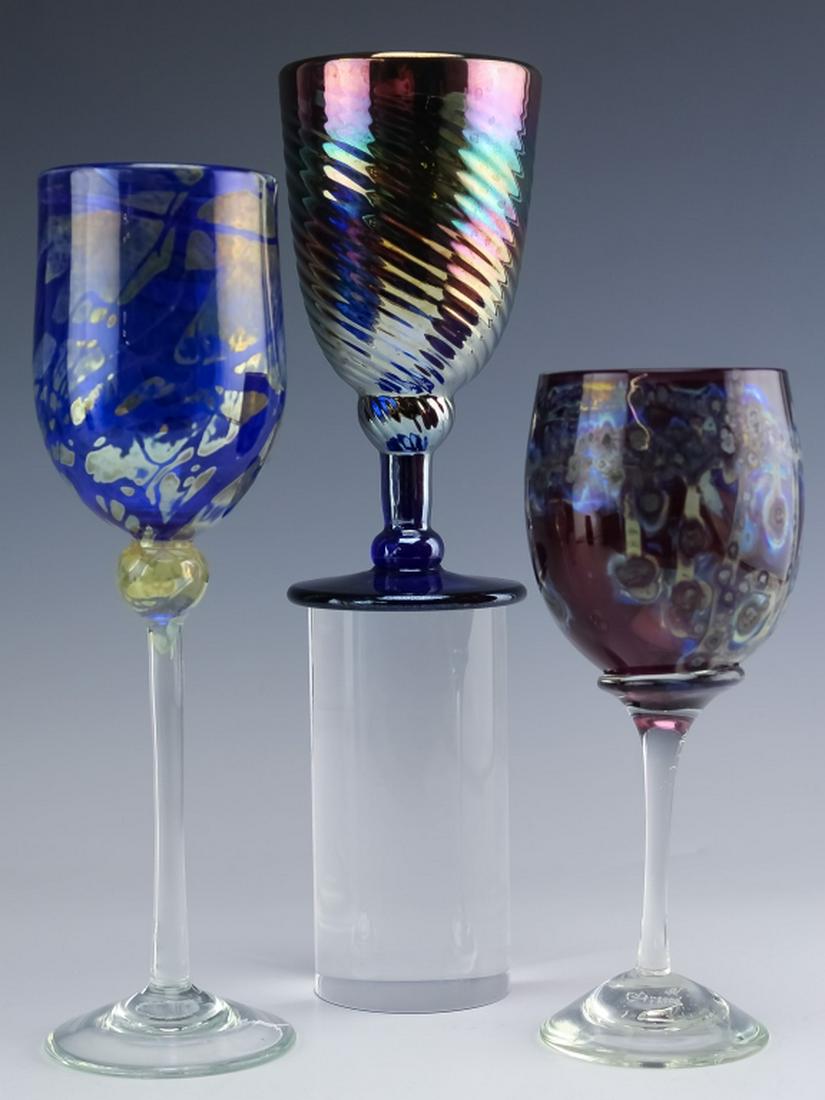 Lot of 3 Signed Studio Art Glass Wine Glasses: Collection of three studio art glass wine stems. Comes with a 10" blue and iridescent stem, a 7 1/4" amethyst and speckled stem, lastly a 6 1/2" iridescent spiral stem. All have a different artist sig