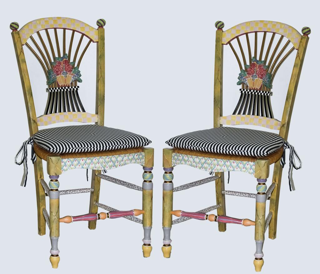 Pair Mackenzie Childs Flower Basket Side Chairs: Pair of table side chairs by Mackenzie Childs. Crafted of hand painted woven rush seats with ceramic art pottery flower basket backs finials and feet. Black And white stripe cushion seat. Features the