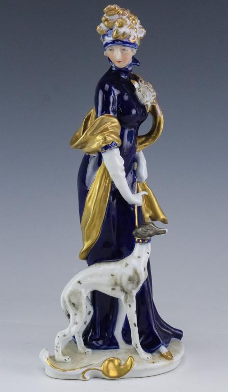 KPM German Porcelain Woman w/ Greyhound Figurine: German porcelain figurine by KPM. Features the form of a woman in cobalt dress with a leashed greyhound to her side. Measures 11" x 4 1/2" x 3 1/2". Marked on base. Good overall condition with minor w