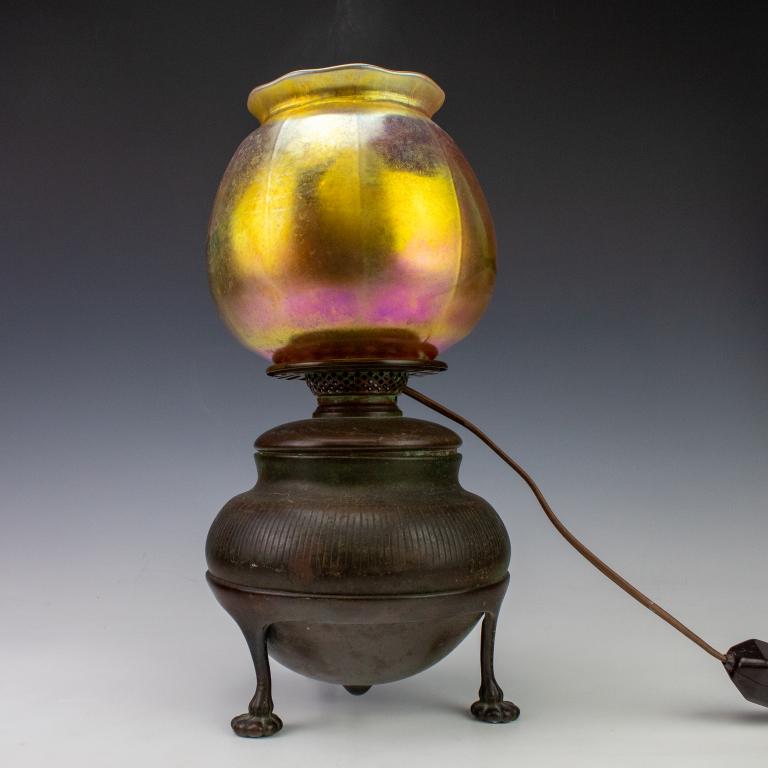 Tiffany Studios Favrille Glass Shade Bronze Lamp: Signed Tiffany Studios table lamp. Crafted of bronze with untouched patina. Tripod footed base in the style of an oil lamp. Mounted with a Favrille glass shade in gold. Oil font impressed Tiffany Stud