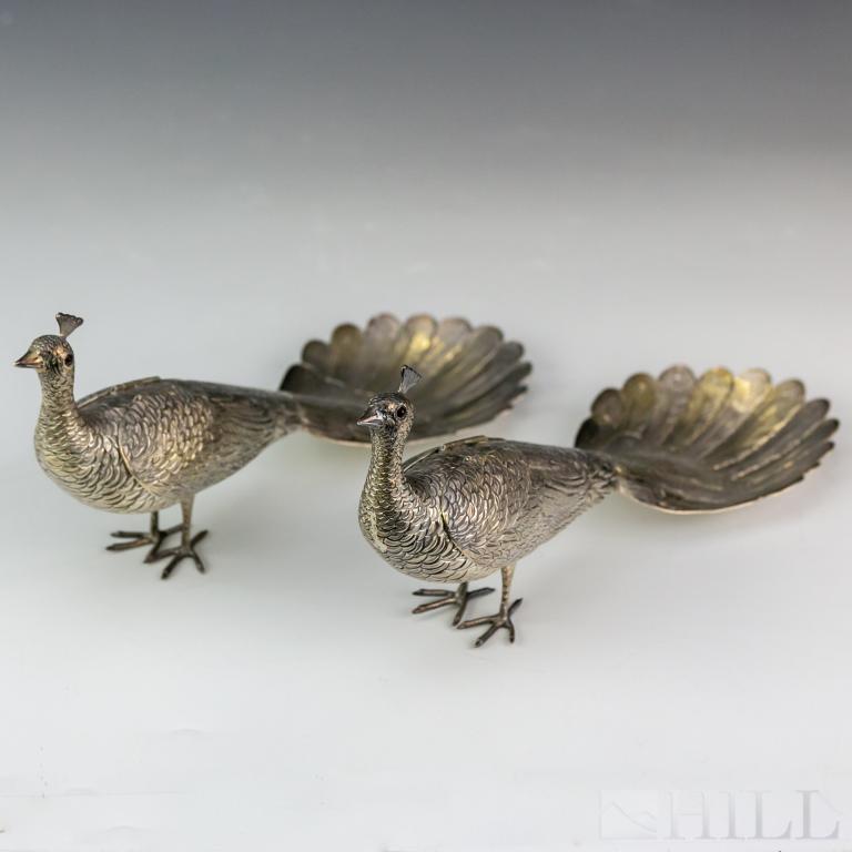 Pair Sterling Silver Peacock Bird Figural Statues: Crafted of sterling silver. Features an exotic peacock bird design. Depicts the male birds with long elegant tail feathers. Hand engraved details and set with glass eyes. Wings hinged to move. Marked 