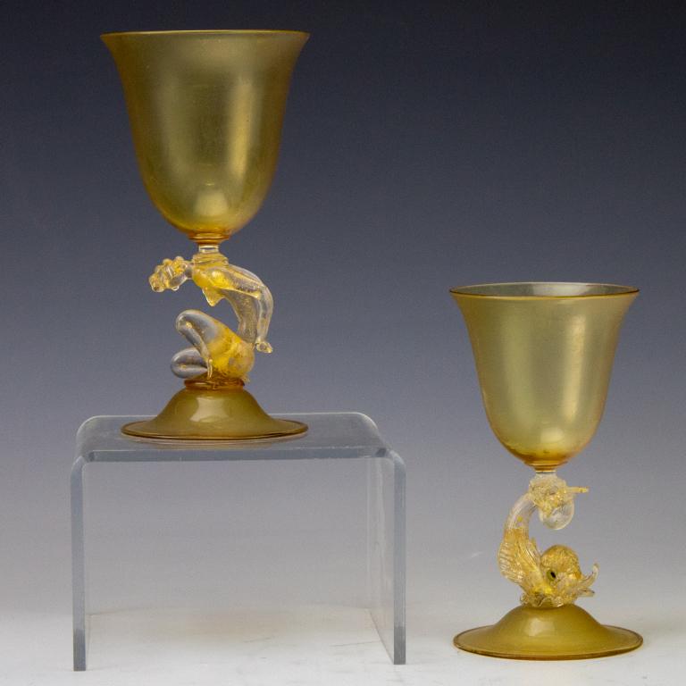 2 Venetian Nude Woman & Dolphin Fish Wine Glasses: Pair of Venetian, Murano Italy art glall wine goblets. Features a kneeling nude woman as won stem and fish form as the second stem. Both have yellow bowls and bases. Measures 7 1/2in. x 4in. & 6 3/4in