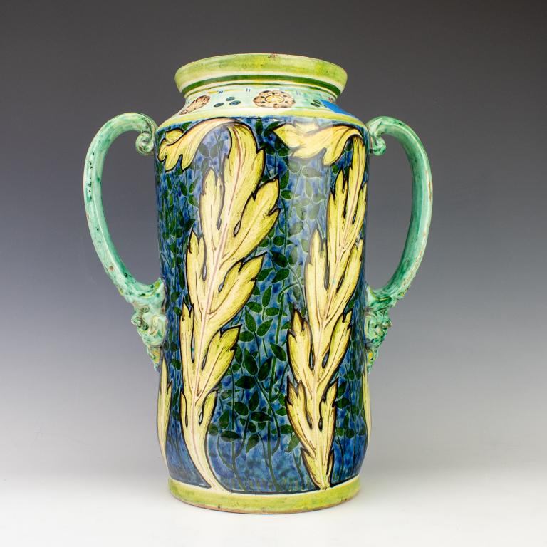 Cassandia Walker Della Robbia English Pottery Vase: Crafted of red ware pottery. Hand painted in gorgeous majolica blue and green family of colors. Art Nouveau style broad leaves against a background of smaller leafy vines. Italian 14th century style d
