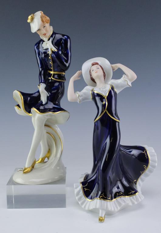 Pair of Royal Dux Porcelain Cobalt Woman Figurines: Pair of porcelain figurines by Royal Dux. Features the form of a woman in a long flowing dress with a hat on, as well as a woman in a shorter dress, also with a hat and gloves. Marked on base. Measure