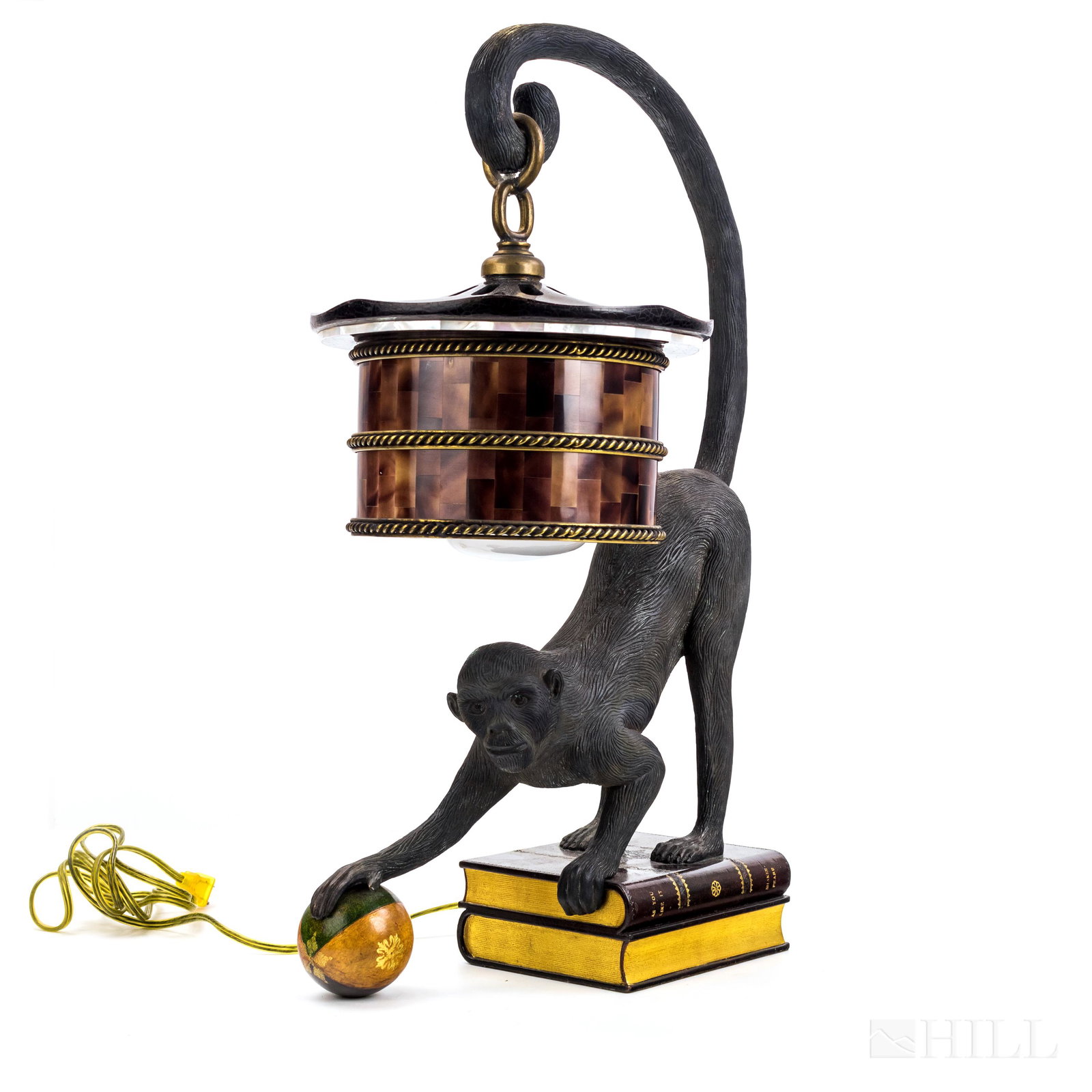 Maitland Smith Bronze Monkey Lantern Table Lamp: Bronze Maitland Smith table lamp. Depicts a monkey standing on a pair of leather bound faux books. He holds a leather ball in one hand and supports a lantern type lamp by his curled tail. Lamp decorat