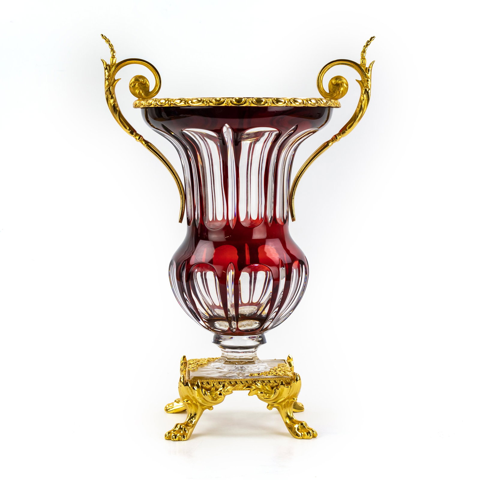 Continental Gold Gilt Ormolu Cut To Clear Urn Vase: Fine quality crystal vase with ormolu mounts. Ruby red cut to clear glass in a classic urn shape. Lion paw footed base with ornate acanthus scroll double handle mounts. Polished bronze with a gold gil