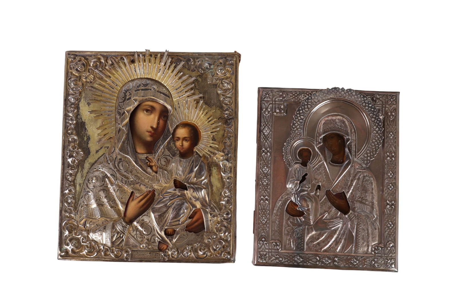 Two Russian Silver Mounted and Painted Icons 490g: Two antique Russian icons depicting the Virgin and Child, each mounted in repousse and engraved silver oklads. Both icons feature hand painted faces and hands with radiating halos, and mounted on a wo