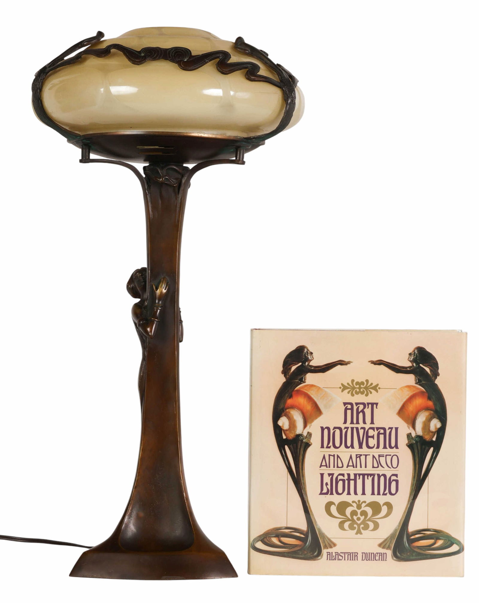 Art Nouveau Gurschner Style Bronze Figural Lamp: Art Nouveau Gurschner-style bronze figural table lamp, featuring a female figure in an embracing pose against a vertical stem element. The lamp is fitted with a shaped cream-colored iridescent glass