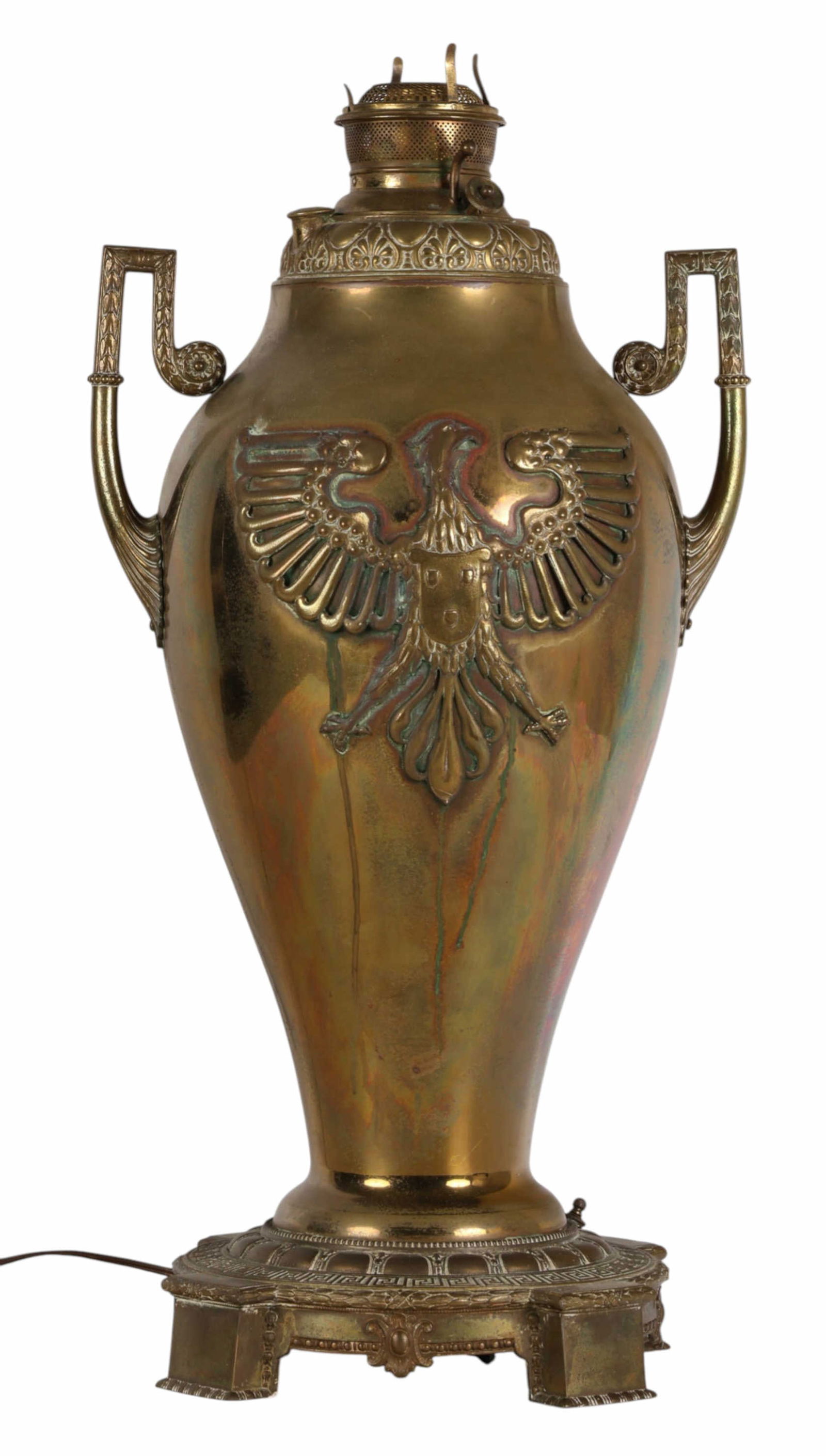 Antique Electrified Brass Oil Lamp w/ Eagle Crest: United States, an early 20th century brass urn form lamp featuring raised double headed eagle motifs on opposing sides. The body is flanked by ornate scroll handles and mounted on a cast base decorate
