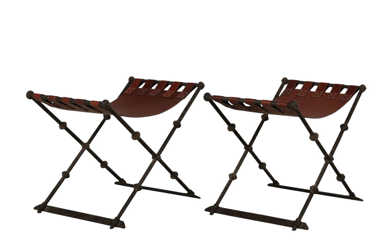 Spanish Revival Pair of Iron Leather Sling Benches: Pair of Spanish Revival hand forged iron X-frame equestrian style stools featuring a patinated, textured hammered finish and cross stretcher supports. Each is fitted with a brown leather sling seat se