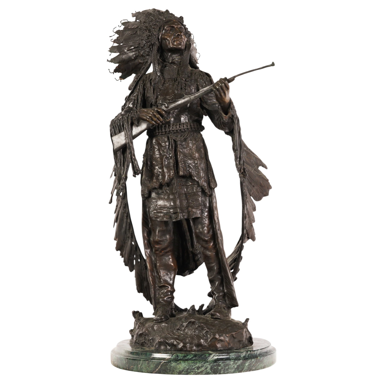 The Indian Chief Bronze Sculpture after Carl Kauba: After Carl Kauba (Austrian, 1865-1922), patinated bronze sculpture depicting a Native American chief standing in ceremonial attire and feathered headdress while holding a rifle. The figure is raised u