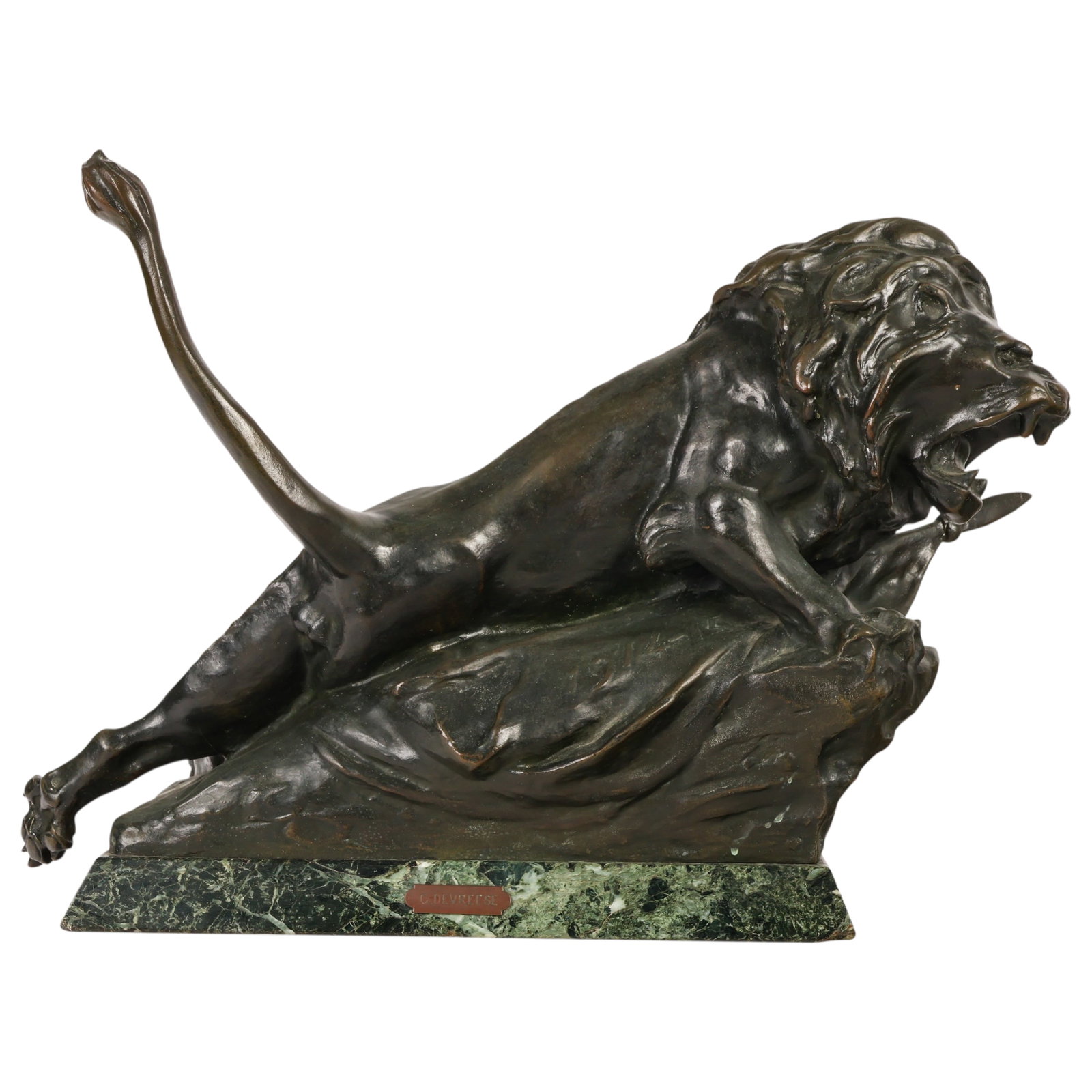 Bronze Fierce Poised Lion Sculpture After Devreese: After Godefroid Devreese (Belgian, 1861-1941), patinated bronze sculpture depicting a roaring lion in a crouching pose atop a naturalistic rocky-form base, with the tip of a flag form projecting benea