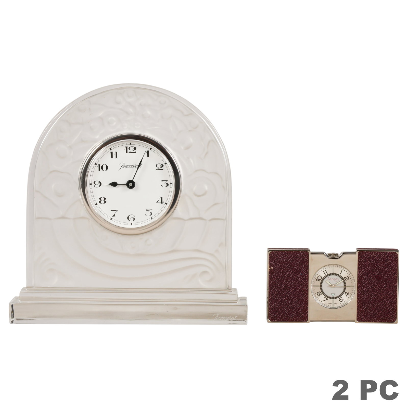 Asprey Travel Alarm Clock & Baccarat Clock 2pc LOT: Lot of two designer clocks comprising one Asprey Swiss-made folding travel alarm clock and one Baccarat crystal desk clock. The Asprey clock features a polished metal case with burgundy embossed leath