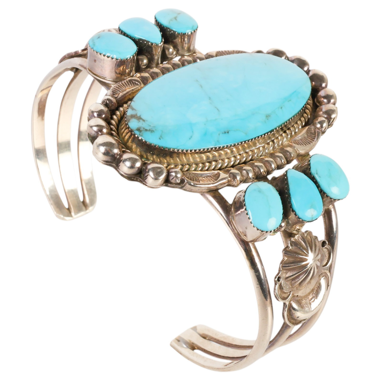 Running Bear Navajo Sterling & Turquoise Bracelet: Turquoise and sterling silver Running Bear Trading Gallup bracelet. Triple banded cuff curves to display large center turquoise stone flanked by six smaller stones. Sides are additionally designed wit