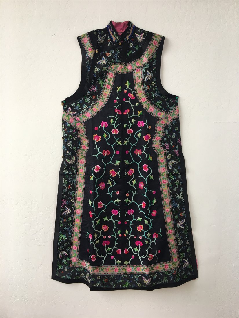 A CHINESE EMBROIDERED SILK LONG VEST: Embroidered with prunus blossoms on a black ground with black silk border bands embroidered with floral sprays and butterflies. 53 inches long.