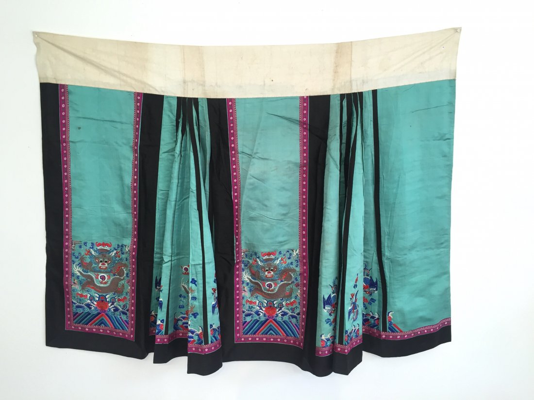 A CHINESE SILK EMBROIDERED SKIRT: Each of the front and back panels embroidered with a dragon in couched gilt threads rising over waves amidst clouds, bats, pearls, and cranes in colorful satin stitches, side pleats embroidered with d