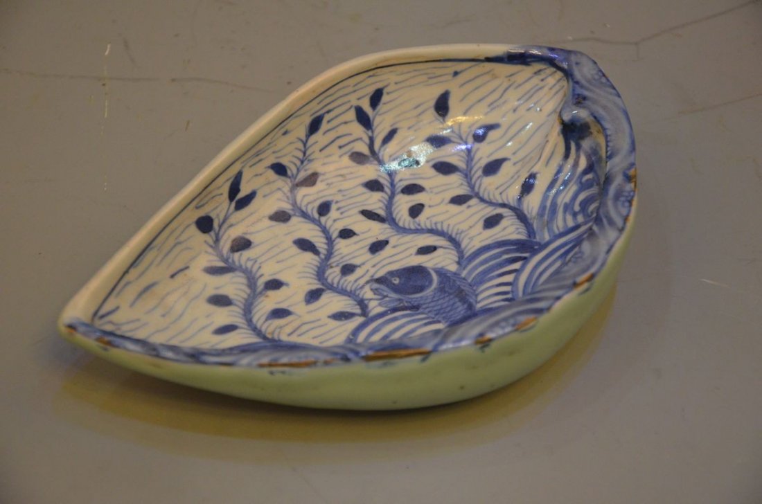 A CHINESE BLUE AND WHITE PORCELAIN BRUSH WASHER: Potted in a tear-drop shape, on the interior painted with a fish swimming amidst waves and aquatic plants, three rounded feet. 8 inches long; 1.5 inches high.