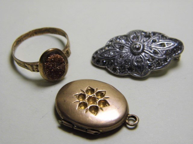 Three Antique Jewelry Elements: A gold plated ring with goldstone setting. Setting is cracked. A pewter and marcasite pin. Pin missing clasp. A patented gold plated locket. May or may not have had settings originally. Locket is wear