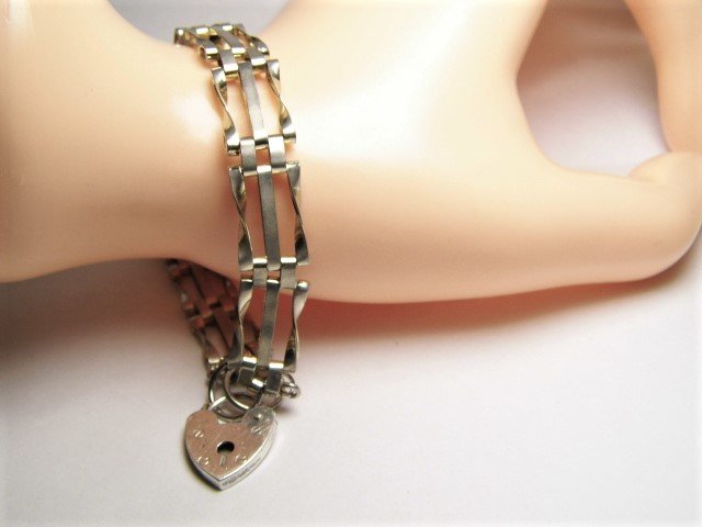 English Sterling Silver Vintage Gate Bracelet: Bracelet length 7 3/4 inches. Heart-shaped lock opens and closes with latch on the side. Full English hallmarks for sterling silver, city of London, date letter is 1978. Silversmith FLo unknown.