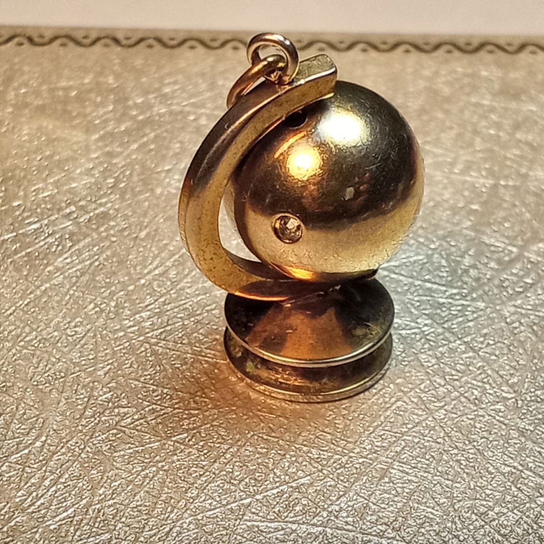 Charm: An atlas sitting on a plinth, and a single little point diamond mounted on it. Marked Trifari underneath with a patent pending. Appears to be silver with a gold wash, but there are no marks for it.
