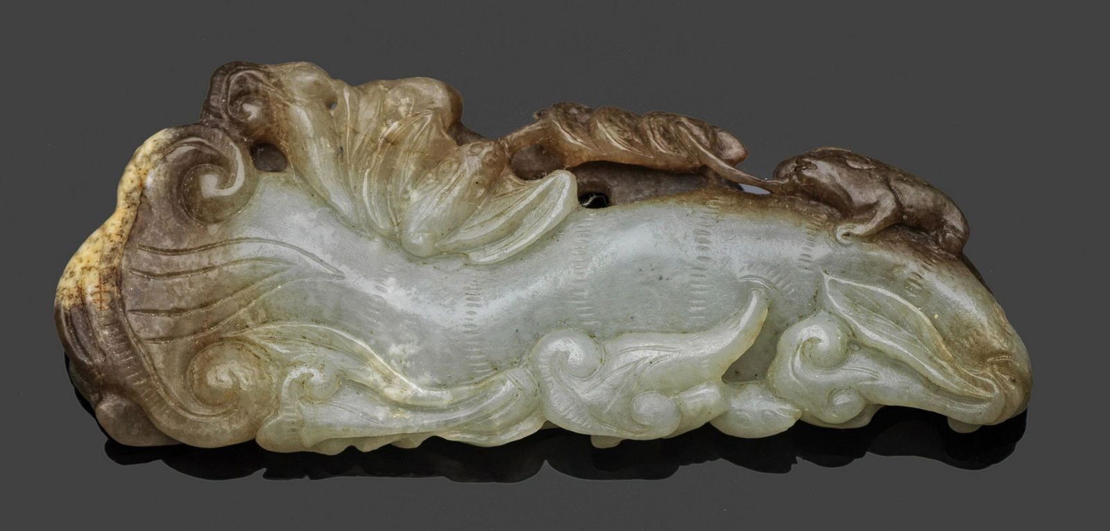 Jadeschnitzerei: Helle seladongrüne bis karamellfarbene Nephrit-Jade. Beidseitig feine Schnitzarbeit in Gestalt eines großen Lingzhi-Pilzes mit Fledermaus (pien fu), dreibeiniger Kröte (hsia ma) und Münzen als Sym