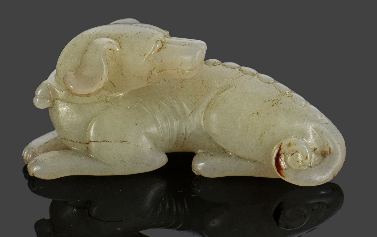 Liegender Hund: Rostbraun geäderte, weiße Hammelfettjade, vollplastisch geschnitzt. L. 7 cm. Provenienz: Asiatika-Sammlung Günther Köpping, Berlin. A carved white and russet veined "mutton fat" jade figure of a r