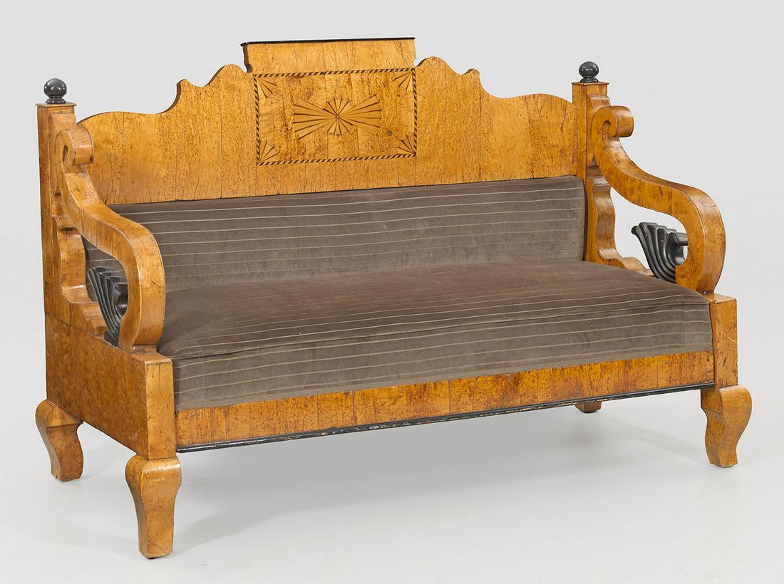 Biedermeier-Sofa: Karelische Birke, furniert und teilw. ebonisiert. Gerade Zarge auf kräftigen, geschweiften Füßen. Stark gebogte Armlehnen aus üppigen Voluten mit Fächerdekor. Geschweift ansteigende Rückenlehnen