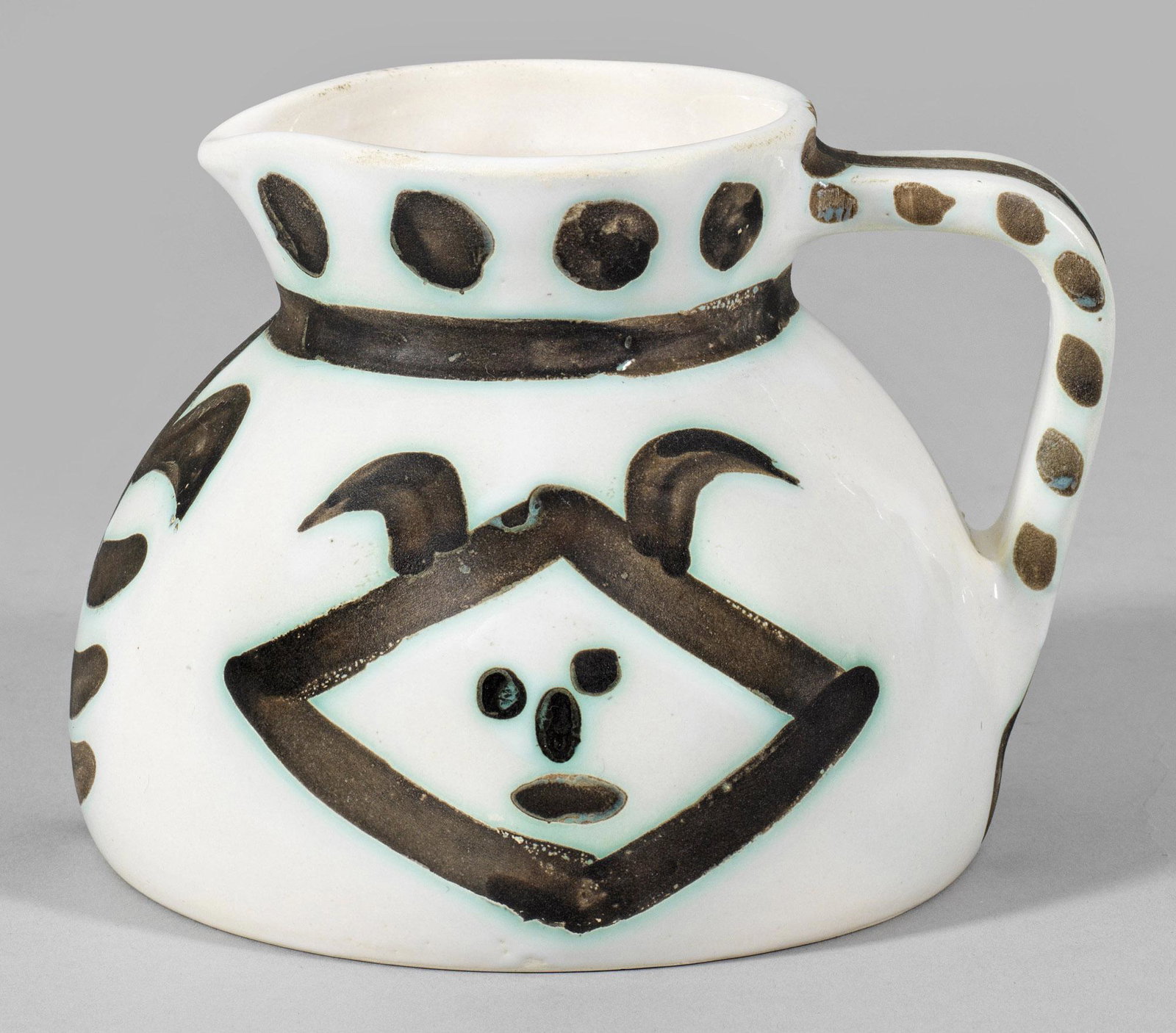 Pablo Picasso: (1881 Málaga - 1973 Mougins) Krug "Têtes" (mit Köpfen). Originaltitel Künstlerkeramik. Irdenware bzw. Fayence mit weißlich-cremefarbener Zinnglasur. Annähernd halbkugelig