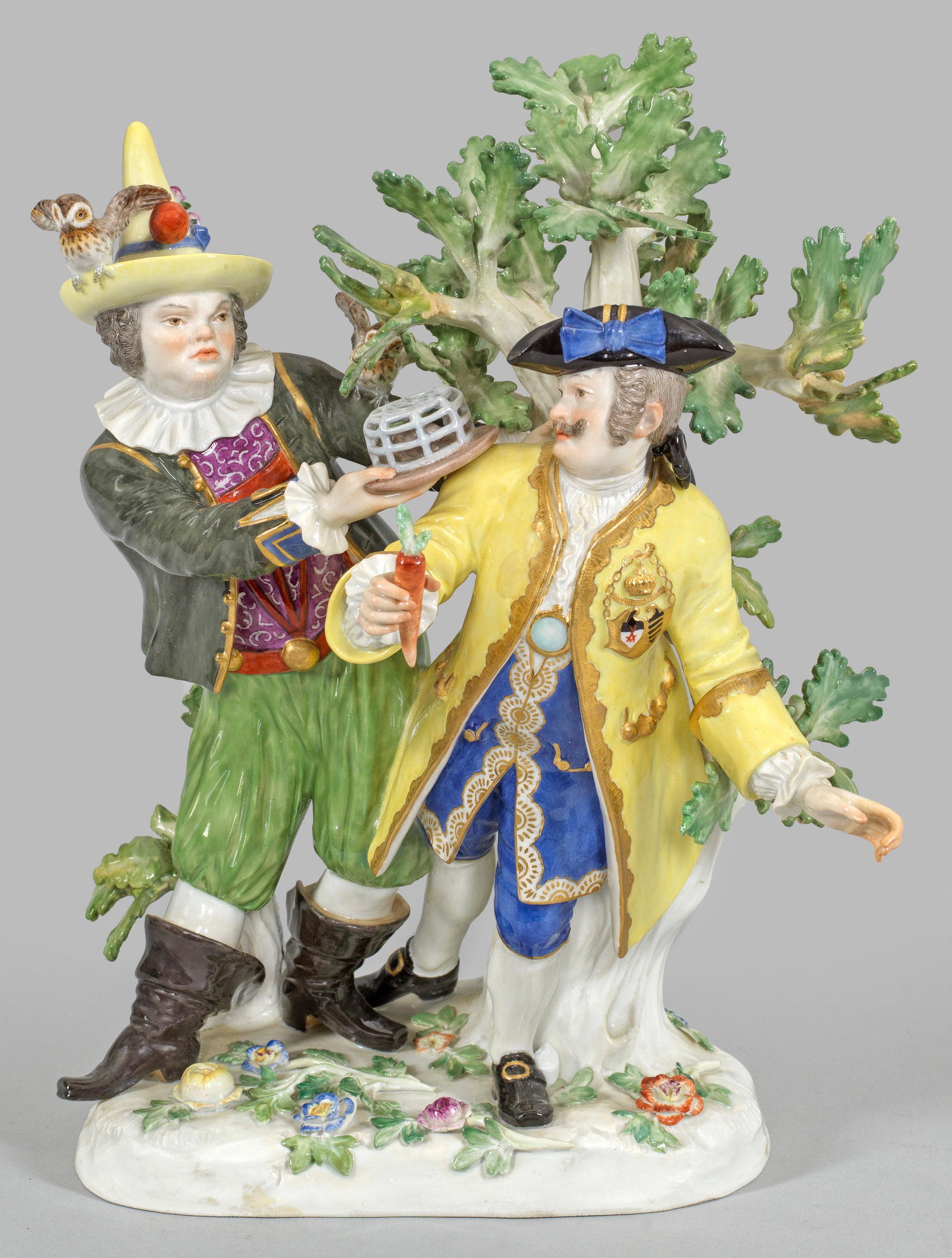 Hofnarr Fröhlich und Schmiedel. Originaltitel: Unregelmäßiger, mit plastischen Blüten und Blättern belegter Sockel. An einem Eichenbaum stehender Hofnarr Fröhlich in farbigem Kostüm, auf seinem Hut eine Eule sitzend. 