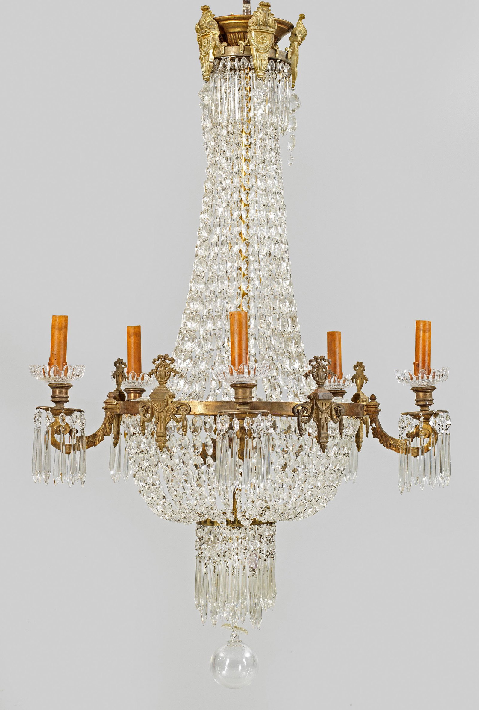 Napoleon III-Deckenlüster: 5-flg.; Bronze, Messing und farbloses Glas. Balusterförmiger Korpus aus Prismenschnüren im Verlauf. In der Mitte schmaler Reif als Träger für blattreliefierte Leuchterarme aus eing