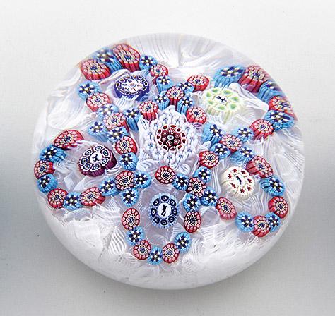 Paperweight "Dentelure/Serration" von Saint-Louis: aus limitierter Edition. Farbloses Glas. Kugelig. Auf weißem "Latticino"-Grund polychrome Darstellung einer Blüte aus Millefiori-Canes. Teilw. mit Silhouette eines Pferdes, eines Hundes, ein