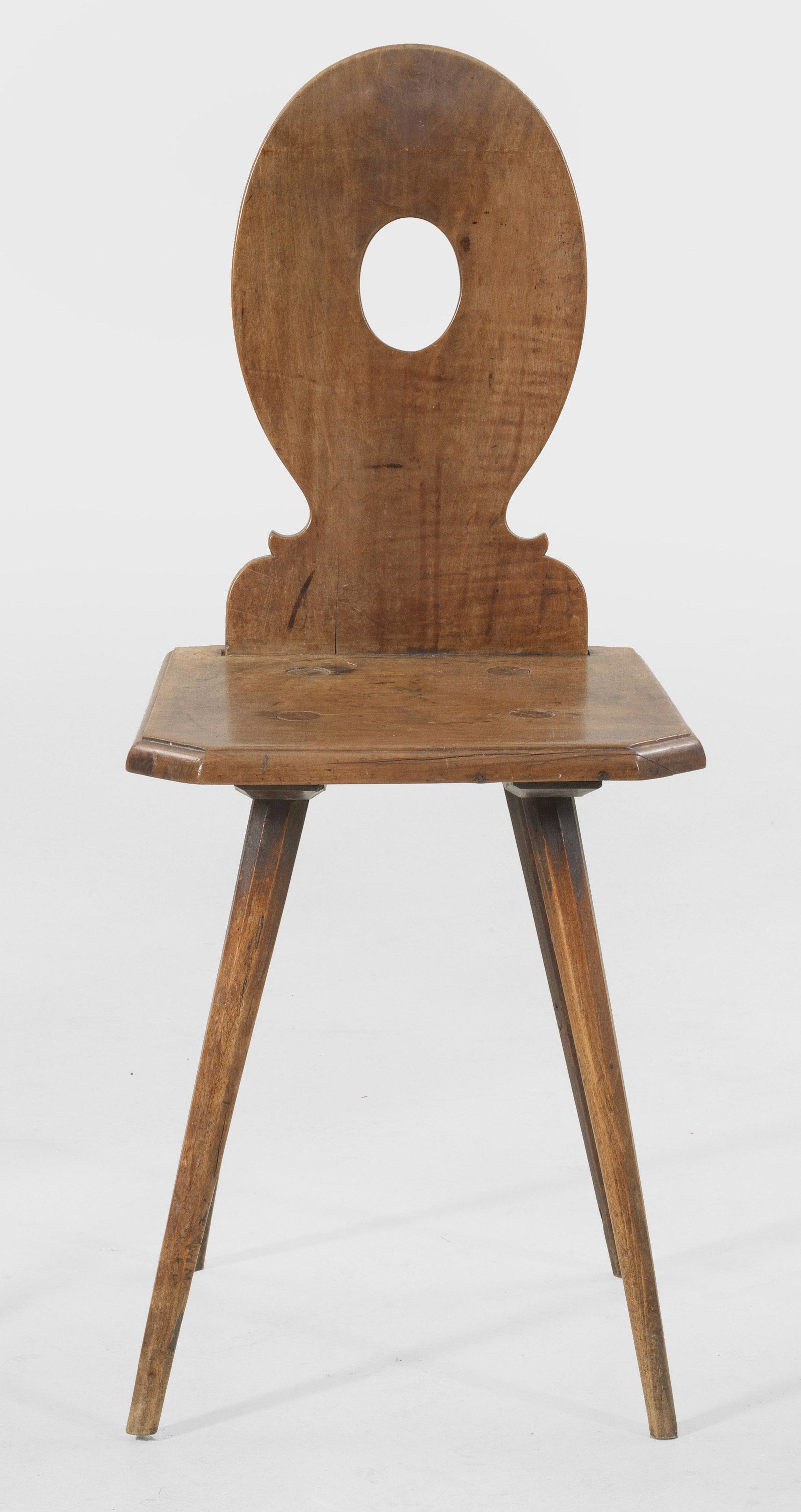 Biedermeier-Brettstuhl: Obstholz und Buchenholz. Flache trapezförmige Sitzfläche auf schräggestellten, spitz zulaufenden, gekanteten Beinen. Balusterförmige, hochovale Rückenlehne mit zentraler Aussp