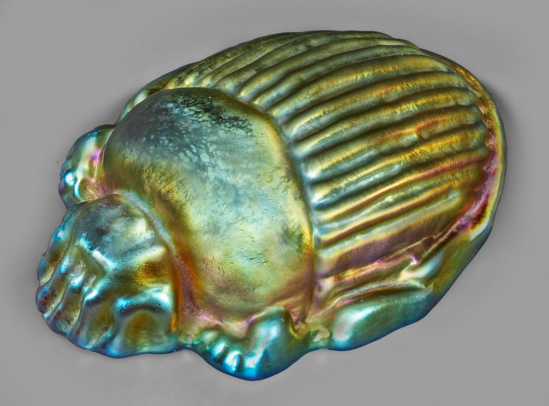 Skarabäus-Briefbeschwerer von Tiffany: Helles, bernsteingelbes Glas, in verschiedenen Tönen irisiert. Sign."L. C. Tiffany Favrile". L. 11 cm. A Louis Comfort Tiffany Studios iridescent Favrile glass scarab paperweight. Signed "L. C. T