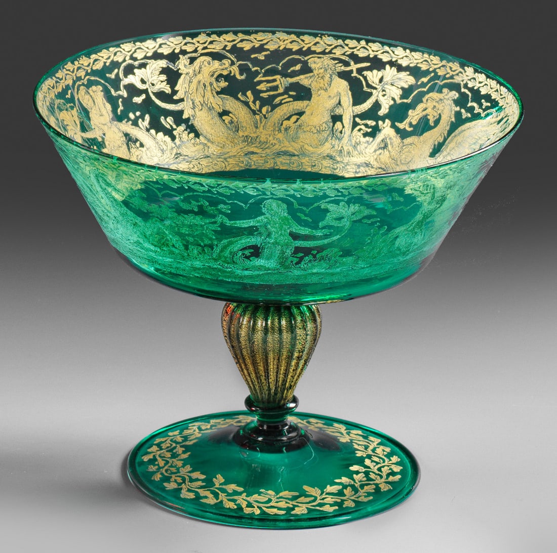 Fußschale im Renaissance-Stil von Gino Cenedese: Grünes Glas. Tellerfuß mit umgeschlagenem Rand, gerippter Balusterschaft mit Goldfolienaufschmelzungen, abgesetzte Kuppa. Radierter Golddekor mit einem Fries aus Neptun, Nixen, Delfin und Me