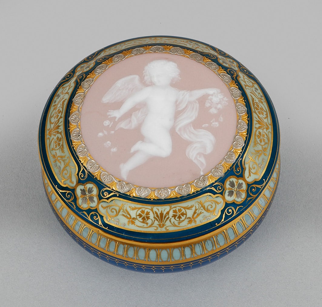 Meissen Pâte-sur-Pâte-Dose: Runder, gebauchter Korpus mit konvex eingezogenem Hals und leicht ausschwingendem Rand. Ansteigender, flach gewölbter Deckel mit ornamentiertem Medaillon. Darin Darstellung eines schwebenden, Bl&