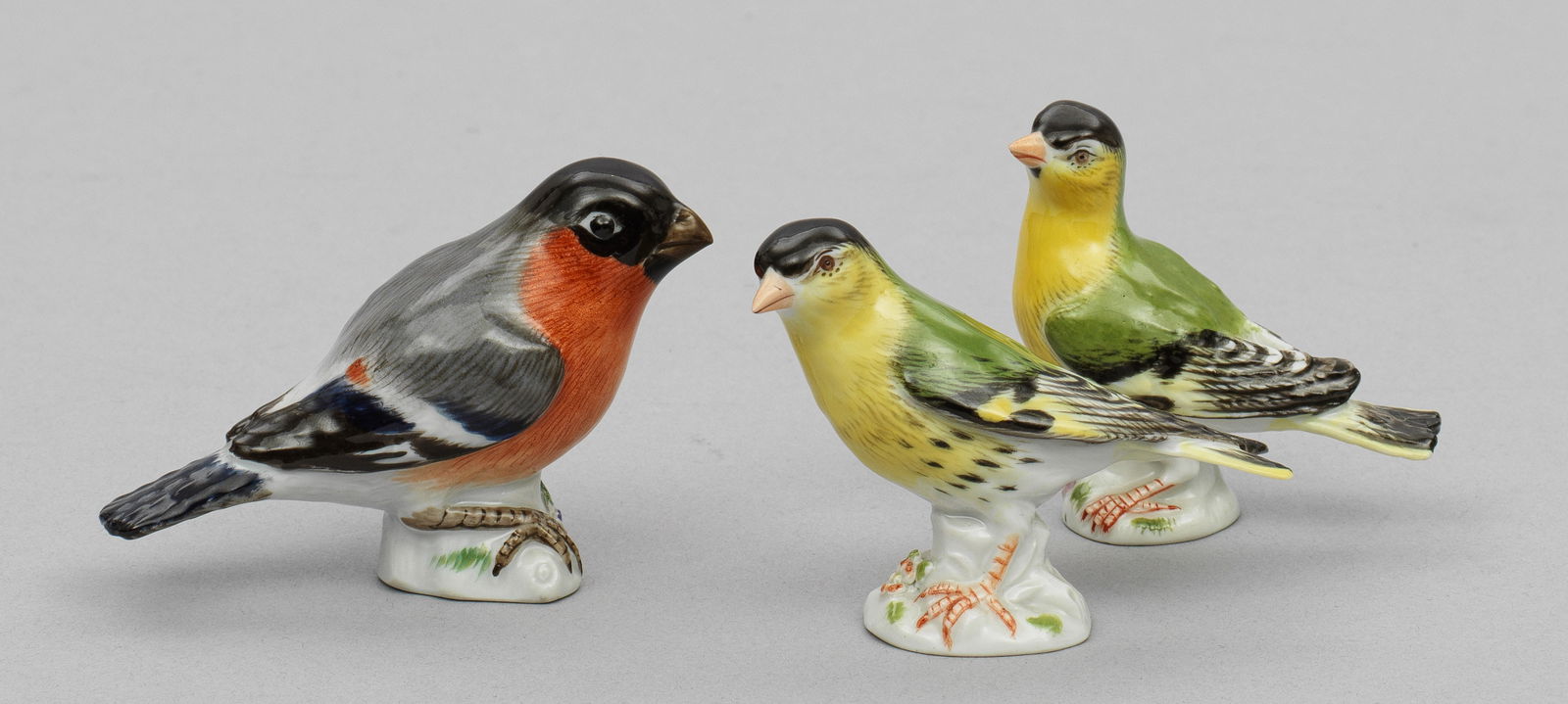 Drei Miniatur-Vögel: Zeissig bzw. Gimpel mit naturalistisch staffiertem Federkleid in polychromer Malerei. Jahreszeichen. Schwertermarke. H. 5,5 cm. Three porcelain bird figures. Date mark. Crossed swords mark. Meissen. U