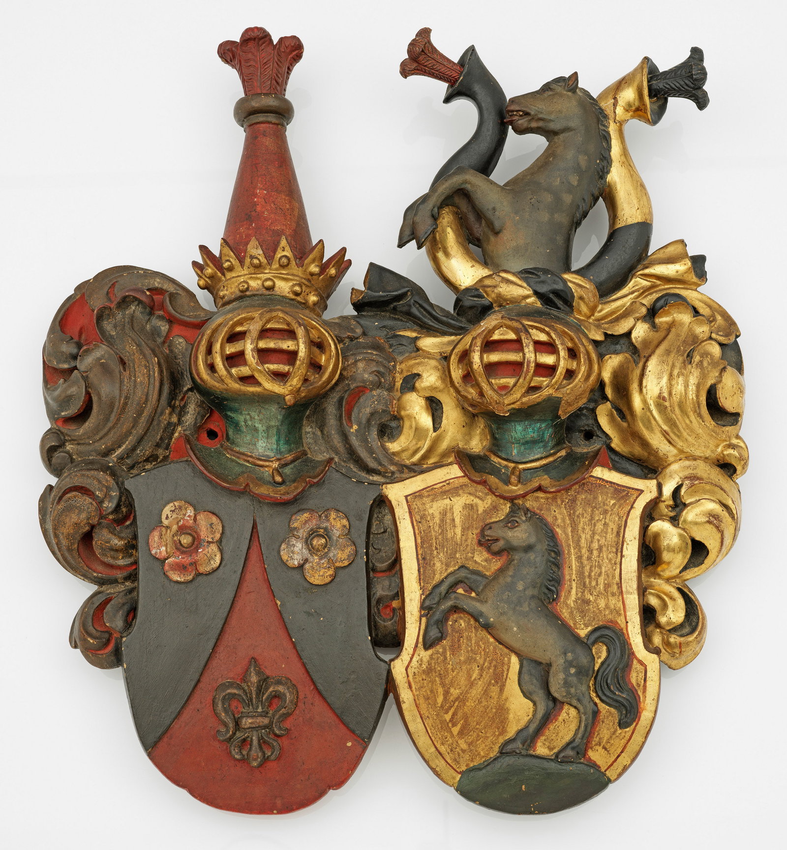 Prächtiges Allianzwappen als Wanddekoration: Nussbaum, geschnitzt sowie polychrom und teilw. mit Gold gefasst. Zwei Wappenkartuschen, gerahmt von üppigem Akanthusblattwerk. Rrechtsseitige Wappenkartusche mit Darstellung eines steigenden Hengste