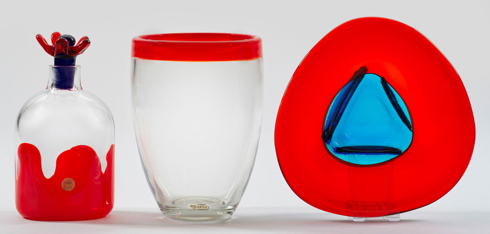 "Carneval"-Glaskaraffe von Christel Holmgren-Exner: mit Stopfen. Entw. Christel Holmgren-Exner, 1970 für Kastrup-Holmegaard Glashütte. Sign., datiert und Firmenetikett. H. 22 cm. Beigaben: dickwandige Glasvase mit Etikett "Mercantile" und eine Glassc