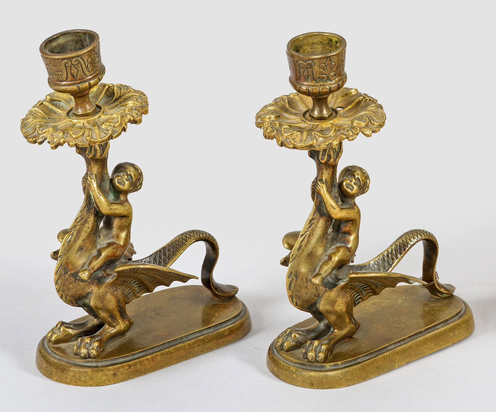 Paar Drachenreiter-Leuchter im Renaissance-Stil: Bronze mit goldbrauner Patina. Auf längsovaler, profilierter Plinthe vollplastische Darstellung eines geflügelten, sog. "Wyvern"-Drachen mit sich an den Hals klammernden Knaben in Traufschale mit ke